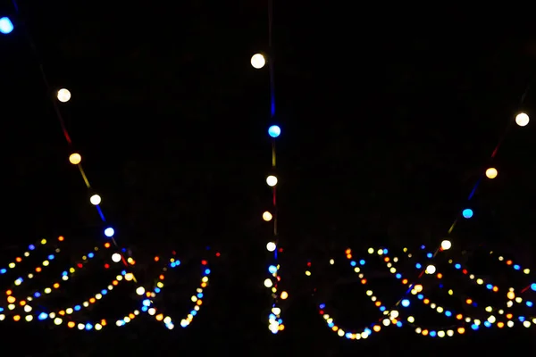 A view from below of a lot of small light bulbs, a festive garland illuminating the night sky