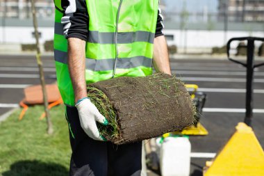 Üniformalı bir işçi elinde yuvarlanmış bir çim tutuyor.