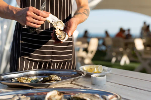 Waiter opens oysters on the summer terrace by the sea
