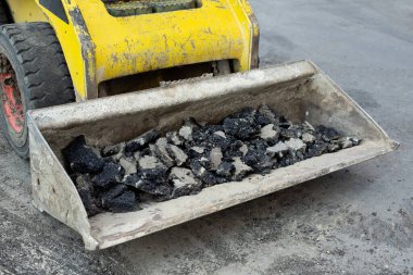 Eski asfaltlı traktör kovası. Yol onarımı çalışıyor