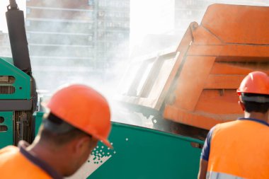 Yeni bir yol inşaatı, bir kamyon asfalt kaldırım taşının kovasına sıcak asfalt döküyor.