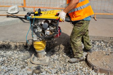 Bir işçi yol tamiri sırasında taşınabilir titreşim tamponu kullanır.