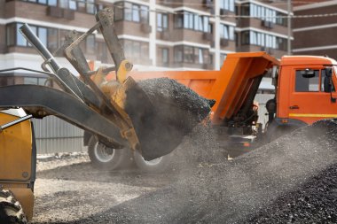 Yeni bir yol inşaatı, kazıcı kovası yolda sıcak asfalt dağıtıyor