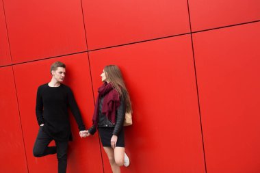 Genç bir adam ve kadın tutkuyla, duygularla, sokakta kırmızı duvarın arka planında. Moda.