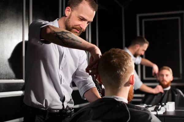 理髪師は理髪店で髪とひげを切ります 美容師ははさみと金属櫛を使用してヘアスタイルを作る — ストック写真