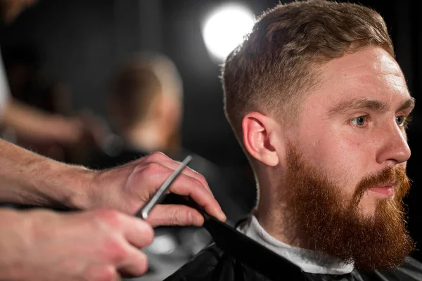 stock image Master cuts hair and beard in the Barber shop. Hairdresser makes hairstyle using scissors and a metal comb