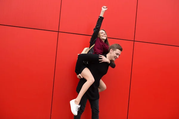 Счастливая Молодая Пара Фоне Красной Стены Девушка Прыгает Парня — стоковое фото