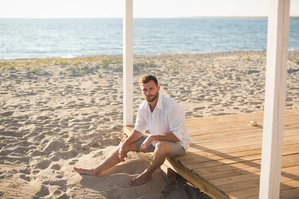 白いシャツを着た男とビーチに座っているショートパンツ — ストック写真