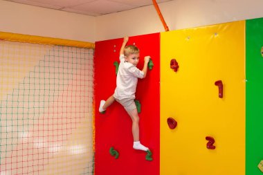 Küçük mutlu çocuk oyun merkezinde duvara tırmanıyor. Çocuklar için kapalı tırmanma kursu