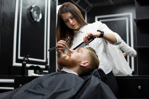 stylist girl shaves beard man in Barbershop