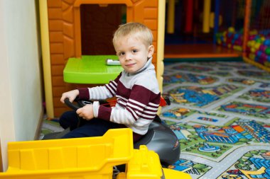 Çocuk evde oyun odasında araba kullanmaktan mutlu.