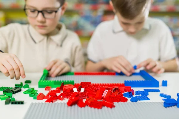 stock image Children play in the designer at the table. Two boys play together with colored plastic blocks in the gaming center, school.