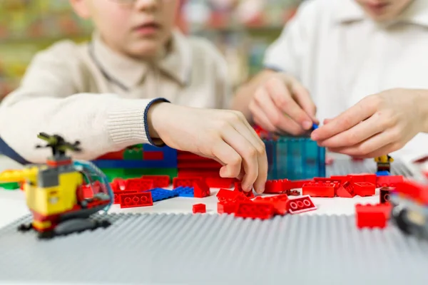 stock image Children play in the designer at the table. Two boys play together with colored plastic blocks in the gaming center, school.