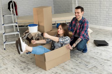 Mutlu çift gülüyor, yeni eve taşınıyor, heyecanlı genç kadın karton kutuda oturuyor, adam onu iterken, neşeli ev arkadaşları eşyalarını yerleştirirken oynuyor.