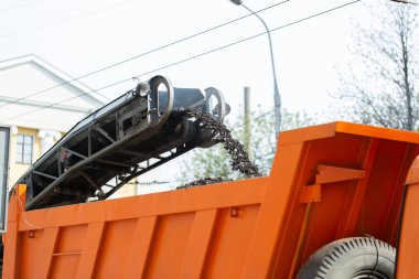 Yol değirmen makinesi eski asfaltı kaldırır ve öğütülmüş asfaltı çöp kamyonuna yükler.