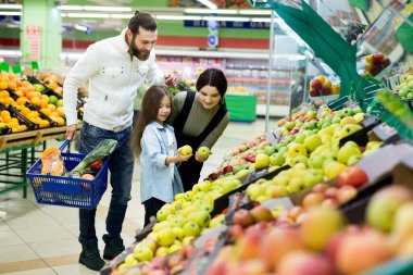 Kızı olan genç bir aile süpermarketteki sebze bölümünden elma seçiyor.