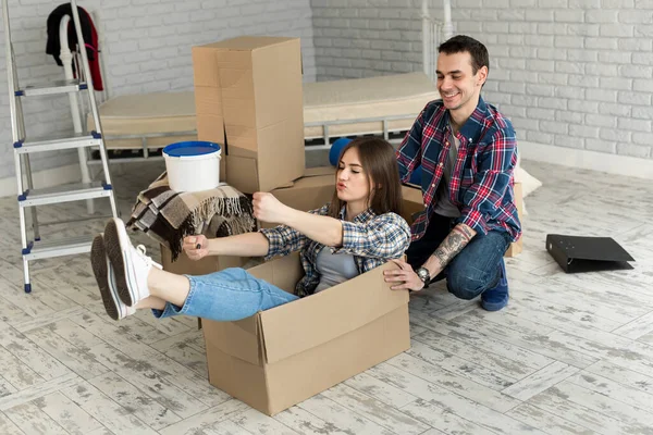 Mutlu çift gülüyor, yeni eve taşınıyor, heyecanlı genç kadın karton kutuda oturuyor, adam onu iterken, neşeli ev arkadaşları eşyalarını yerleştirirken oynuyor.