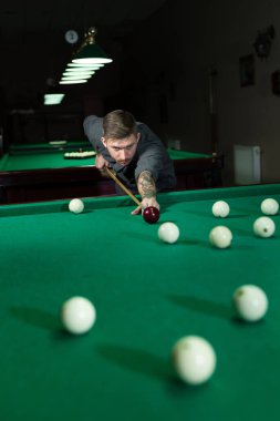Adam bilardoda topa vurmaya çalışıyor. Arka planda bilardo odası.