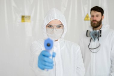 Korunaklı kıyafet uzmanları Coronavirus salgını sırasında Covid-19 test merkezinde temassız ateşi ölçüyor..
