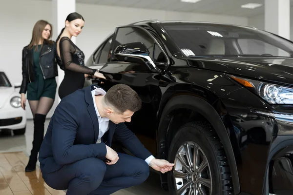 stock image Attractive elegant man examining wheels of a new automobile on sale at dealership. Handsome male driver choosing new car to buy