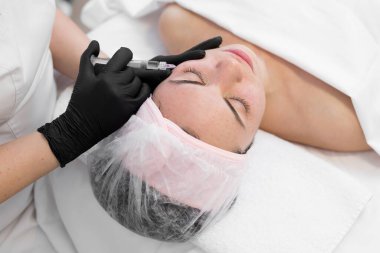 Kozmetik uzmanı genç bir kıza yaşlanma karşıtı iğneler yapıyor. Güzellik uzmanımız yüzdeki biyoevrizma prosedürünü uygular. Enjeksiyondan elde edilen kan ciltte görünür.