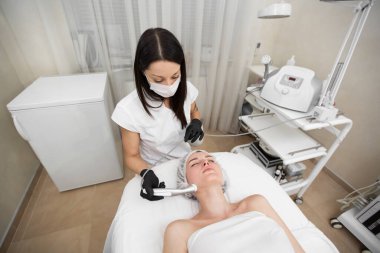 Spa salonundaki genç bir kız için enjeksiyonsuz mezoterapi prosedürünün en üst noktası. Güzellik uzmanı modaya uygun kızlara modern yaşlanma karşıtı tedaviler uyguluyor.