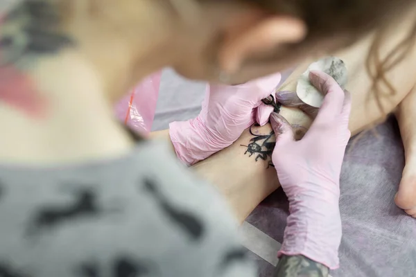 サロンの若い女の子の足に入れ墨をするタトゥーアーティストのクローズアップ スタジオで入れ墨を行うプロのタトゥー師 — ストック写真