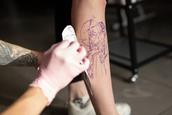 Cropped shot of tattoo artist transferring tattoo sketch on shoulder in tattoo salon