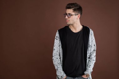 Depresyondaki genç adam. Şık erkek öğrenci yuvarlak gözlük takıyor, modaya uygun saç stiline sahip, kendine güvenen, kahverengi arka planda soyutlanmış görünüyor. İnsanlar ve insan ifadeleri