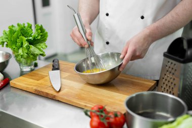 Şef, sebzeli omlet yapmak için elleriyle yumurta çırpıyor.