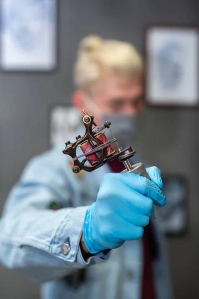プロのタトゥーアーティスト青手袋の男はタトゥーマシンを保持しています スタジオで入れ墨を作成するワークフロー — ストック写真