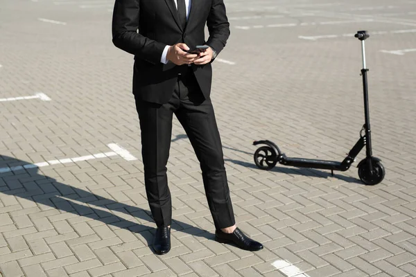 スーツの若いハンサムなビジネスマンが電動スクーターに乗って電話を見て — ストック写真