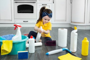 Küçük kız mutfağı temizlerken sprey tabancayla oynuyor.