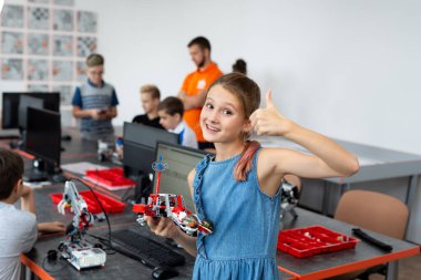 Portre öğrencisi kollarında robot tutuyor. Robot bilimi dersinde bir bilgisayara programlanmış plastik parçalardan bir araya getirilmiş.