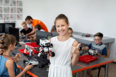 Robot bilimleri dersinde mutlu bir liseli kızın portresi, bir bilgisayarda programlanmış plastik parçalardan bir robot tutuyor.