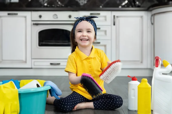 A little girl is playing with cleaning products at home in the kitchen