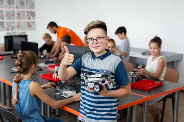 Robot derslerinde bir araya getirdiği robotla mutlu bir okul çocuğunun portresi, çocuk baş parmağını gösteriyor.