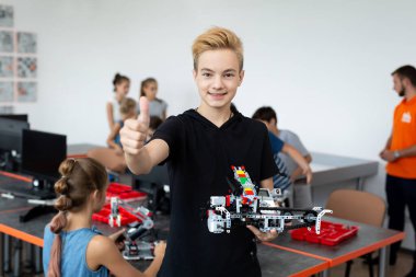 Robot derslerinde bir araya getirdiği robotla mutlu bir okul çocuğunun portresi, çocuk baş parmağını gösteriyor.