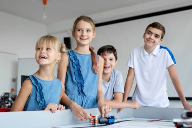 Okulda robot bilimi dersinde arka planda bilgisayarları olan modern bir ofisi olan mutlu çocukların portresi.