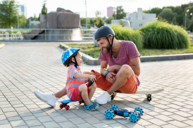 Kasklı mutlu baba ve oğul, kaykayların üzerinde otururken eldivenle kontrol edilen robot bir arabayla parkta oynuyorlar..
