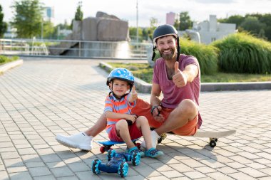 Kasklı mutlu baba ve oğul, kaykayların üzerinde otururken eldivenle kontrol edilen robot bir arabayla parkta oynuyorlar..