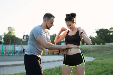 Gün batımında stadyumda genç bir kadının belini bir mezura ile ölçer.