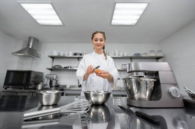 Bir pasta şefinin elleri profesyonel bir mutfakta bıçakla yumurta kırar..