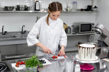 Pasta şefi pastayı süslemek için çilek keser.