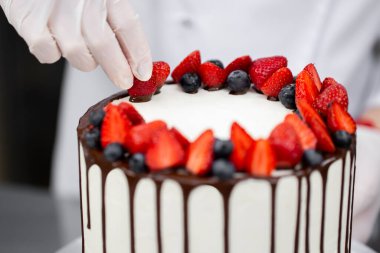 Pasta şefi pastayı çilek ve çikolatayla süslüyor..