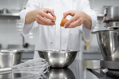 Bir pasta şefinin elleri profesyonel bir mutfakta yumurta kırar..