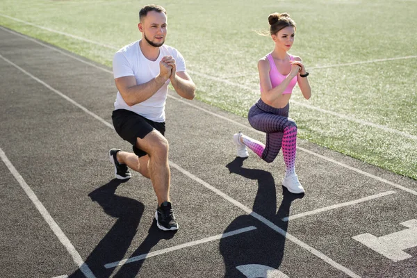 Man and a woman play sports at the stadium in the summer, making lunges