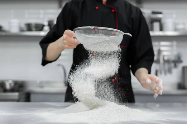 stock image The pastry chefs hands sift the flour through a sieve on the table.