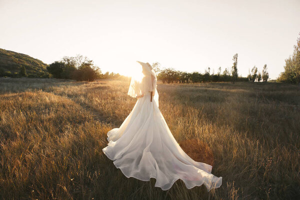 Portrait of a gentle bride in a straw hat and a veil of a veil at sunset.
