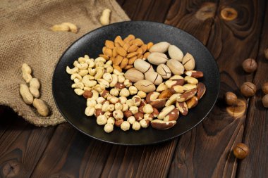 Kahverengi ahşap arka planda siyah bir tabakta fındık karışımı.